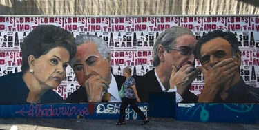 A woman walks past a mural depicting the president of the Brazilian lower house of Congress Eduardo Cunha (2-R) speaking with the president of the Brazilian Social Democracy Party (PSDB) Aecio Neves (R) as if they were conspiring against Brazilian President Dilma Rousseff (L), who is depicted speaking with Vice-President Michel Temer, at Paulista Avenue in Sao Paulo, Brazil on April 19, 2016.Brazil woke Monday to deep political crisis after lawmakers authorized impeachment proceedings against President Dilma Rousseff, sparking claims that democracy was under threat in Latin America's biggest country. / AFP / NELSON ALMEIDA (Photo credit should read NELSON ALMEIDA/AFP/Getty Images)