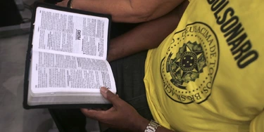 18 October 2018, Brazil, Rio de Janeiro: A man with a T-shirt with the inscription "Bolsonaro" reads the Bible during the last evangelical mass before the election in Brazil. Bolsonaro is receiving an additional boost from the evangelical movements in Brazil, which support his conservative agenda. Photo: Ian Cheibub/dpa (Photo by Ian Cheibub/picture alliance via Getty Images)