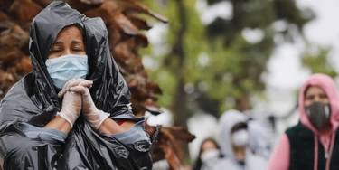 Juana Gomez, à esquerda, usa máscara, luvas, e um saco de lixo para se proteger da chuva na fila de espera em um centro de distribuição de alimentos durante a pandemia do coronavírus, no dia 9 de abril de 2020, em Van Nuys, na Califórnia.