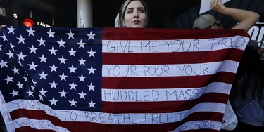 LOS ANGELES, CA - JANUARY 29: Chella, from Sherman Oaks, holds the U.S. flag with words from the sonnet, "The New Colossus," by poet Emma Lazarus  while joining people who continue to protest President Donald Trump's travel ban at the Tom Bradley International Terminal at LAX on January 29, 2017 in Los Angeles, California. The poem is attached to the Statue of Liberty. Chella only goes by her first name. (Photo by Genaro Molina / LA Times via Getty Images)