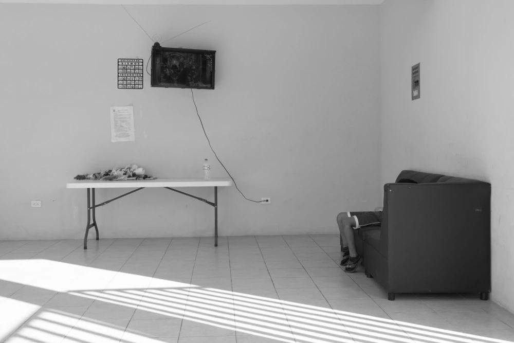 A seven-year-old boy watches television at a refuge for families seeking asylum in Tapachula, Chiapas. The television has only two channels and there are few toys at the shelter.His family fled El Salvador after gang members threatened to kill his eldest brother for witnessing another teenager's murder. The brother refused to join the gang and hid in a closet with a false ceiling when gang members came looking for him. After several months, his mother left her house carrying almost nothing, as if she was going for a walk, and fled the country with her three sons. They now live in a shelter for asylum-seekers as their application for refugee status is processed. They're grateful for the refuge, but the donated food is often scarce and they are allowed to leave just once a day and must be back by 6:00PM. They are terrified that gang members will spot them, as the city is full of migrants from El Salvador.