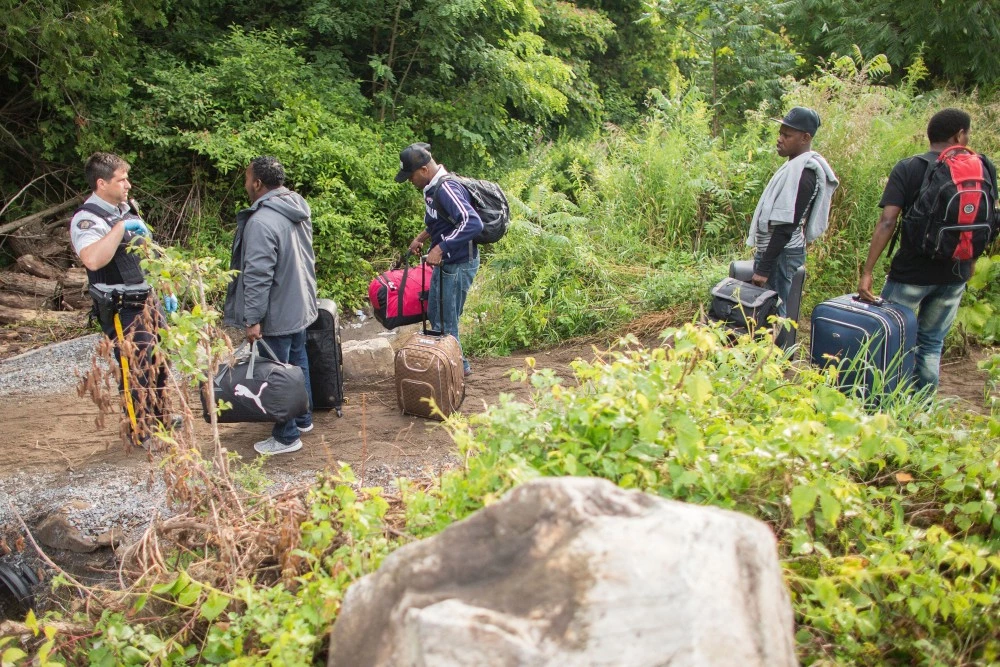 An RCMP officer talks with a group of people who claimed to be from Haiti in Champlain, New York as they prepare to cross the border into Canada illegally on August 4, 2017.Migrants have been crossing the border in greater numbers in recent weeks. / AFP PHOTO / Geoff Robins (Photo credit should read GEOFF ROBINS/AFP/Getty Images)