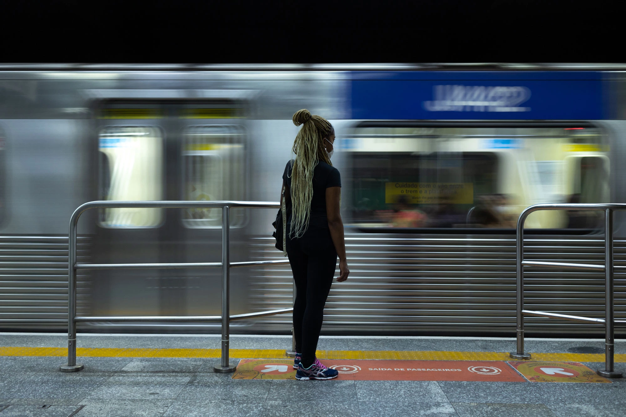 A caminho do trabalho, no centro de São Paulo.Jéssica Alves Maia do Rio Branco, 24 anos. Presta serviço de faxineira desde os 16 anos para aplicativos, empresas e clientes particulares, em jornadas que podem chegar até 12h de trabalho. Em sua casa, no Jardim Peri, na Zona Norte de São Paulo, é responsável pelos cuidados de sua mãe, que é paraplégica, e de sua avó. Para se deslocar de sua residência aos locais de trabalho leva até 3h de transporte público, entre ônibus, metrôs e trens. Seu sonho é ser médica e atualmente está tentando uma vaga para escola militar.