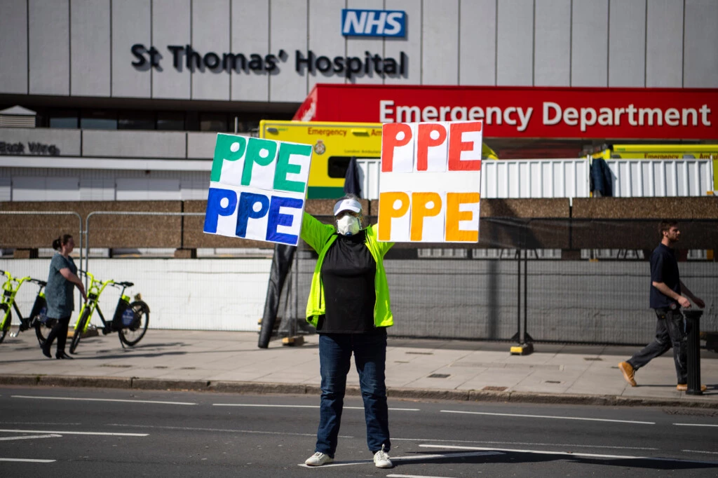 Uma mulher segura um cartaz com os dizeres "PPE" [EPI] diante do Hospital St. Thomas, em 7 de abril, em Londres.