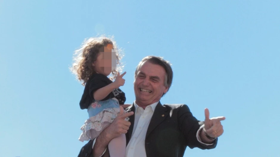 Bolsonaro ensina menina a fazer uma arma com a mão.