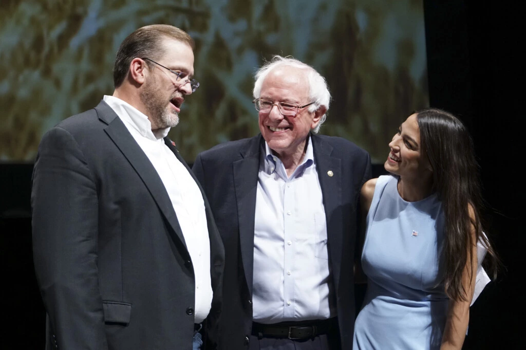 James Thompson, candidato do Partido Democrata ao Congresso pelo Kansas, à esquerda; Senador Bernie Sanders, Independente por Vermont; e Alexandria Ocasio-Cortez, candidata do Partido Democrata ao Congresso por Nova York se reúnem no palco depois de um comício em Wichita, no Kansas, em 20 de julho de 2018.