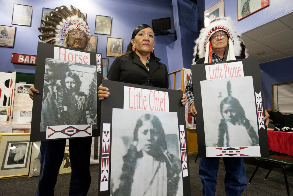 Yufna Soldier Wolf, ao centro, Mark Soldier Wolf, à esquerda, e Crawford White pai mostram fotos das três crianças do povo Arapaho do Norte enterradas na Carlisle Indian School durante uma reunião para negociar o repatriamento dos restos mortais de 10 crianças na Reserva Rosebud, em Rosebud, Dakota do Sul.