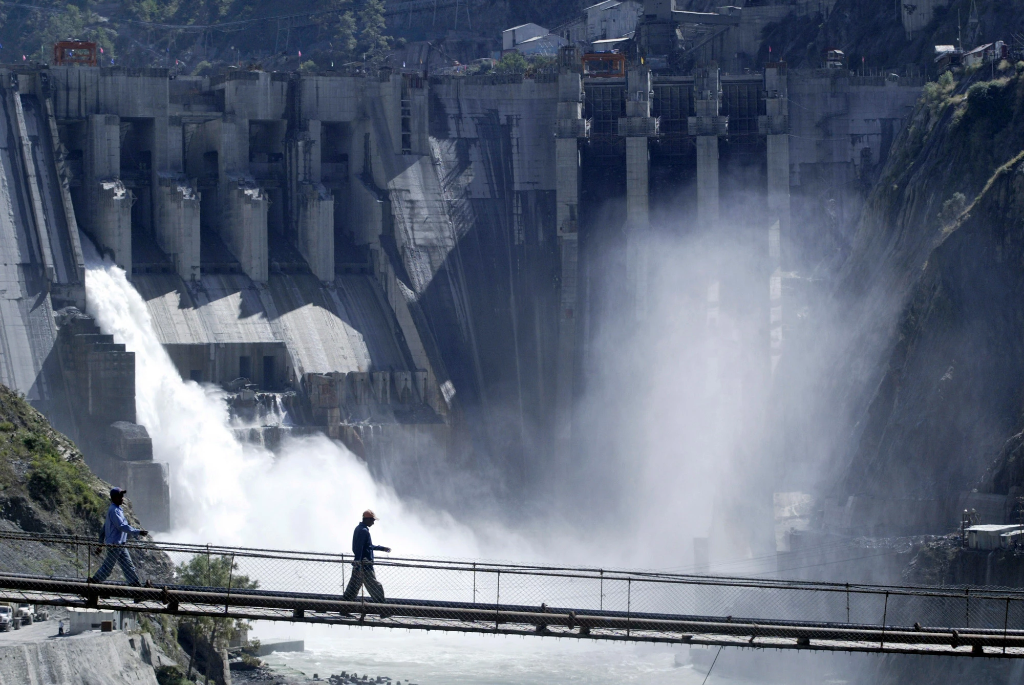 Trabalhadores caminham em uma ponte tendo ao fundo o projeto hidroelétrico de 450 MW de Baglihar, construído no rio Chenab, em Chanderkot, cerca de 154 quilômetros ao norte de Jammu, Índia, 10 de outubro de 2008.