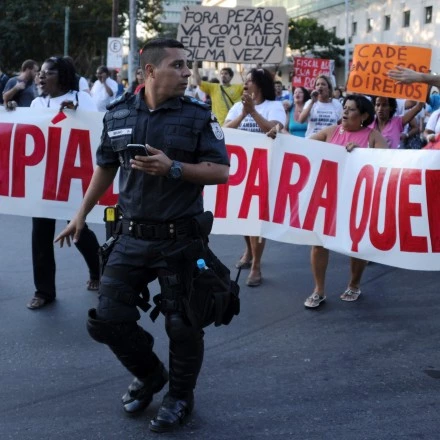 Demonstrators hold a banner reading "Olympics for whom?" next to a policeman during a protest against the Rio 2016 Olympic Games in Rio de Janeiro, Brazil on August 5, 2015.       AFP PHOTO / TASSO MARCELO        (Photo credit should read TASSO MARCELO/AFP/Getty Images)