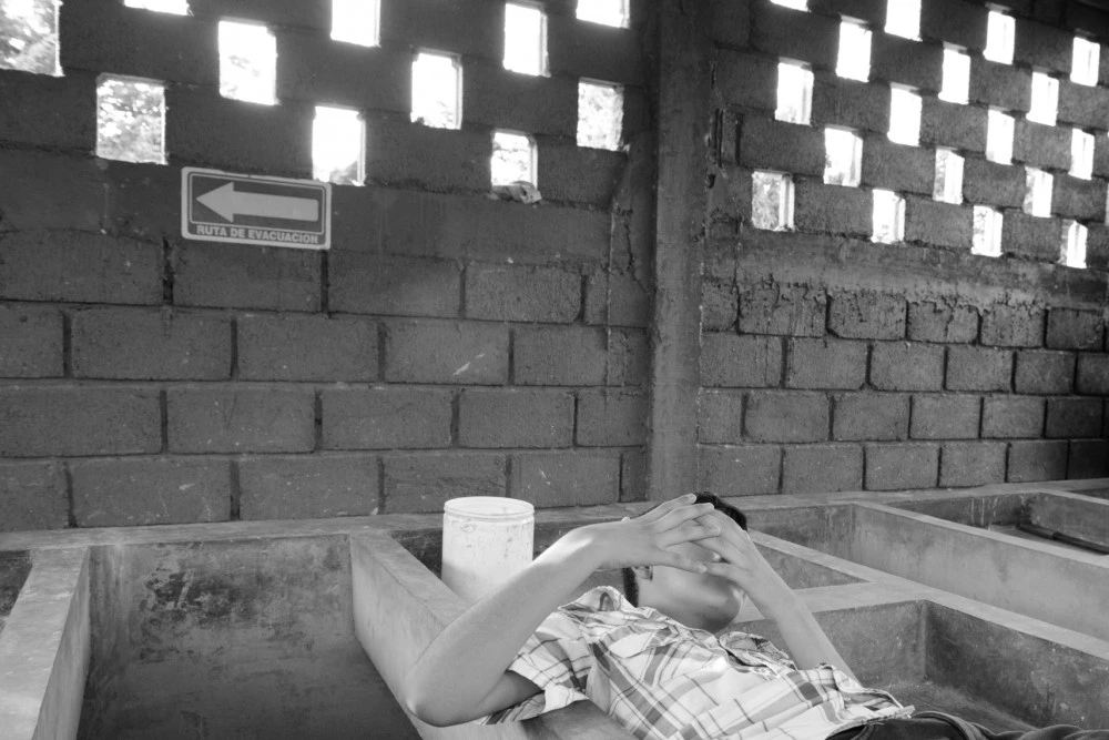 A 13-year-old Honduran boy reclines in a sink for washing clothes at a refuge for families seeking asylum in Tapachula, Chiapas. Gang members killed his father, a police officer, six years ago. They demanded his mother hand over half of the money she earned selling food on the street, then later insisted the boy join the gang or his 15-year-old sister become their girlfriend, so the family fled.They now live in a shelter for asylum-seekers as their application for refugee status is processed. They're grateful for the refuge, but the donated food is often scarce and they are allowed to leave just once a day and must be back by 6:00PM. They are terrified that gang members will spot them, as the city is full of migrants from Honduras.