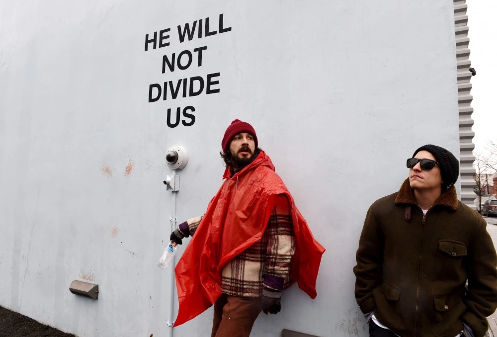 US actor Shia LaBeouf(L)is seen during his He Will Not Divide Us livestream outside the Museum of the Moving Image in Astoria, in the Queens borough of New York January 24, 2017 as a protest against President Donald Trump. LaBeouf has installed a camera at the Museum of the Moving Image in New York that will run a continuous live stream for the duration of Trumps presidency. LaBeouf is inviting the public to participate in the project by saying the phrase, He will not divide us, into the camera. / AFP / TIMOTHY A. CLARY (Photo credit should read TIMOTHY A. CLARY/AFP/Getty Images)