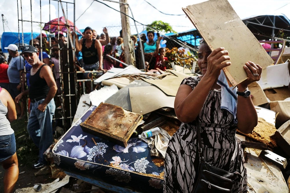 SAN ISIDRO, PUERTO RICO - OCTOBER 17:  A woman shields her face from the sun with a piece of wood as residents wait to receive food and water, provided by FEMA, in a neighborhood without grid electricity or running water on October 17, 2017 in San Isidro, Puerto Rico. The food and water delivery mission included U.S. Army, U.S. Coast Guard and Puerto Rico Hacienda forces. Residents said this was the first official governmental delivery of food and water to the community, nearly four weeks after the hurricane hit. Puerto Rico is suffering shortages of food and water in areas and only 17.7 percent of grid electricity has been restored. Puerto Rico experienced widespread damage including most of the electrical, gas and water grid as well as agriculture after Hurricane Maria, a category 4 hurricane, swept through.  (Photo by Mario Tama/Getty Images)