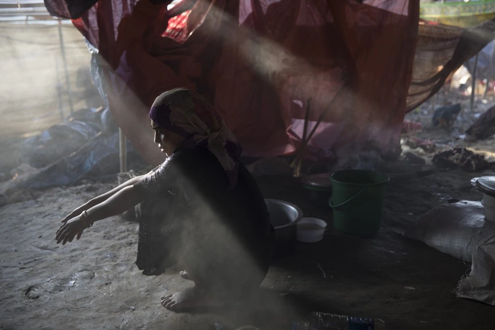 THAINKHALI, BANGLADESH - SEPTEMBER 25:  Sajida Begum, 18, sits in her makeshift tent, washing rice for dinner as smoke catches the late afternoon light September 25, 2017 in Thainkhali camp, Cox's Bazar, Bangladesh. Over 429,000 Rohingya refugees have fled into Bangladesh since late August during the outbreak of violence in Rakhine state as Myanmar's de facto leader Aung San Suu Kyi downplayed the crisis during a speech in Myanmar this week faces and defended the security forces while criticism on her handling of the Rohingya crisis grows. Bangladesh's prime minister, Sheikh Hasina, spoke at the United Nations General Assembly last week, focusing on the humanitarian challenges of hosting the minority Muslim group who currently lack food, medical services, and toilets, while new satellite images from Myanmar's Rakhine state continue to show smoke rising from Rohingya villages.  (Photo by Paula Bronstein/Getty Images)