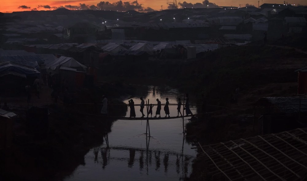 KUTUPALONG, BANGLADESH - OCTOBER 13: People cross a bamboo bridge over a stream as the sun sets on October 13, 2017 at the Kutuplaong refugee camp, Cox's Bazar, Bangladesh. According to UN sources around 519,000 Rohingya refugees had fled across the border from Myanmar to Bangladesh since 25 August. Thousands more remain stranded in Myanmar without the means to cross the border into Bangladesh. (Photo by Paula Bronstein/Getty Images)