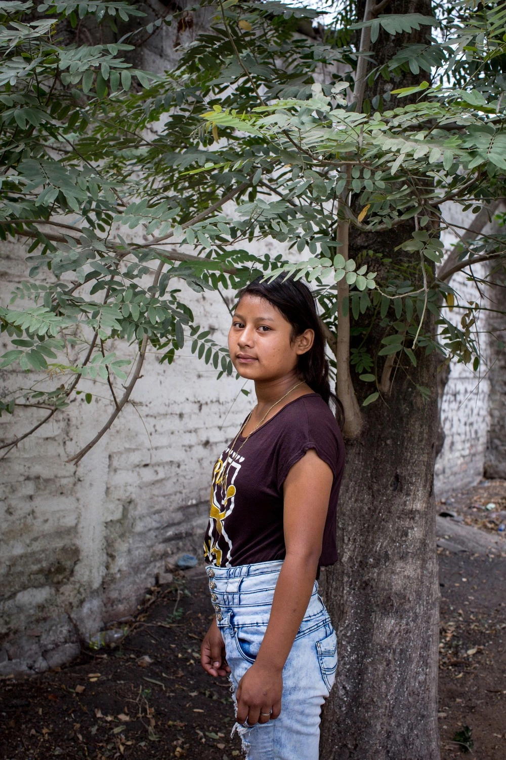April 2017, El Salvador, San Salvador. Natalie Martinez, 15, poses for a portrait near the soccer field she used to play on in her neighborhood of San Salvador. She had to quit soccer because she works nights and weekends now whenever she's not in school at a local mechanic shop. Several of her brothers are gang members and she says they live in constant fear that the family will be attacked by police. She says she fears the police more than any other gang. "I had a friend who was really pretty once. Karin. She was 15. A gangster wanted her but she rejected him. He took her one day. After that they found her dead. "She says she is afraid to leave her home a lot of the time. (Natalie Keyssar)