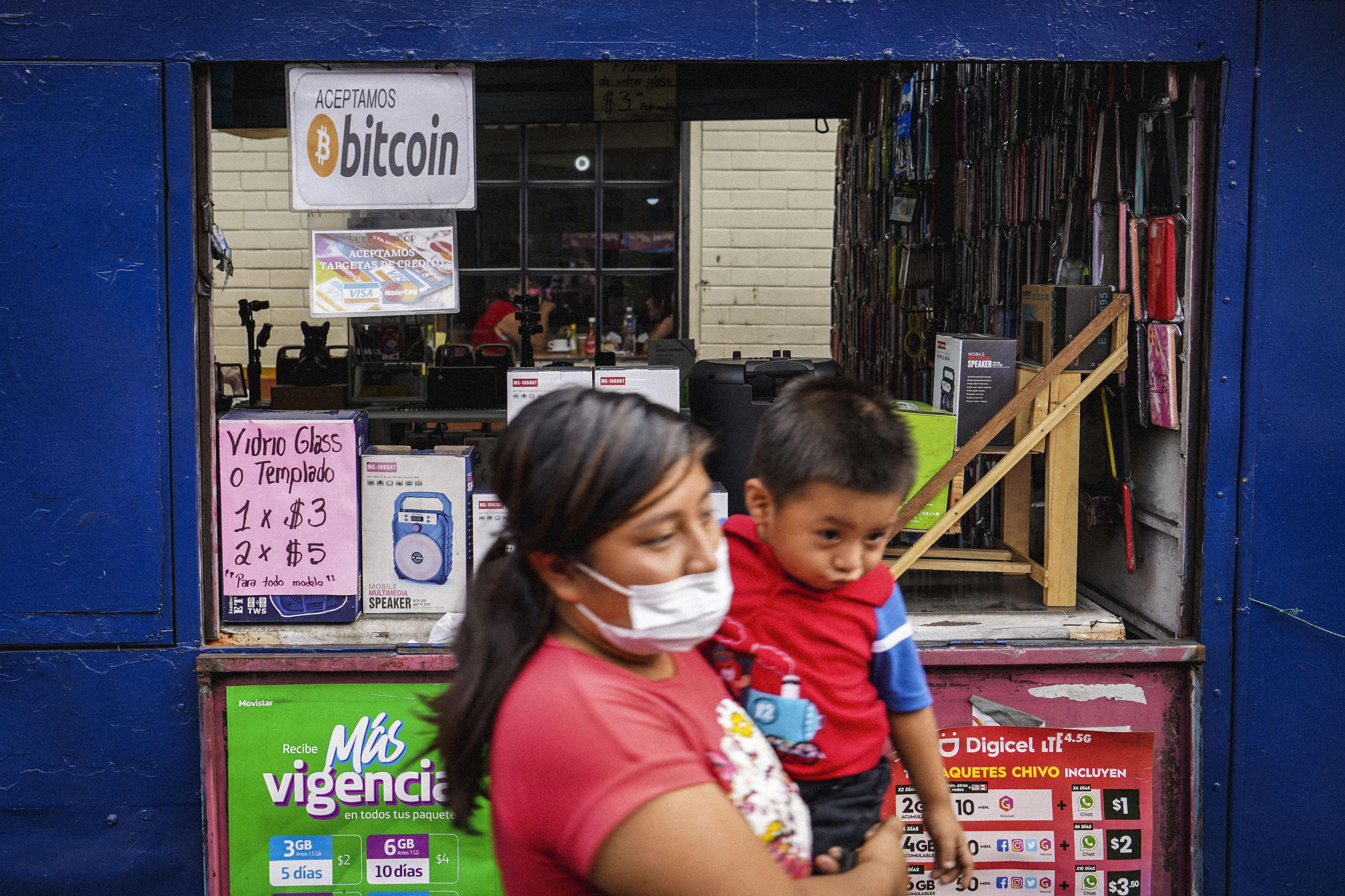 A woman carrying a child walks next to a sign displaying the acceptance of Bitcoin as a payment method on June 15, 2022 in San Salvador, El Salvador. El Salvador´s government has experienced losses of half of it´s $103 million US Dollar investement in Bitcoin as Bitcoin´s price fell to around $20,000 US Dollars. (Photo by Camilo Freedman/NurPhoto via Getty Images)