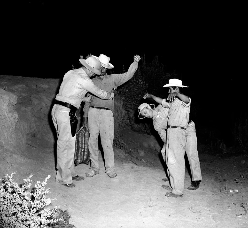 Inspetores da Patrulha de Fronteira dos EUA, do quartel-general do setor de El Centro, revistam dois mexicanos, logo depois de os dois homens cruzarem ilegalmente a fronteira com o México em 11 de agosto de 1951.