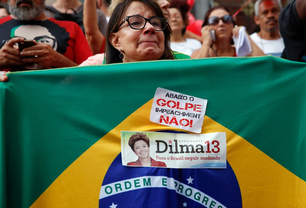 A demonstrator holds a Brazilian flag with a sticker that reads in Portuguese "Down with the coup, impeachment no" during a protest in support of Brazil's President Dilma Rousseff and former President Luiz Inacio Lula da Silva in Sao Paulo, Brazil, Thursday, March 31, 2016. Rousseff is currently facing impeachment proceedings as her government faces a stalling national economy and multiple corruption scandals. Lula da Silva has been linked to a sprawling corruption scandal involving Brazilian oil giant Petrobras. (AP Photo/Andre Penner)