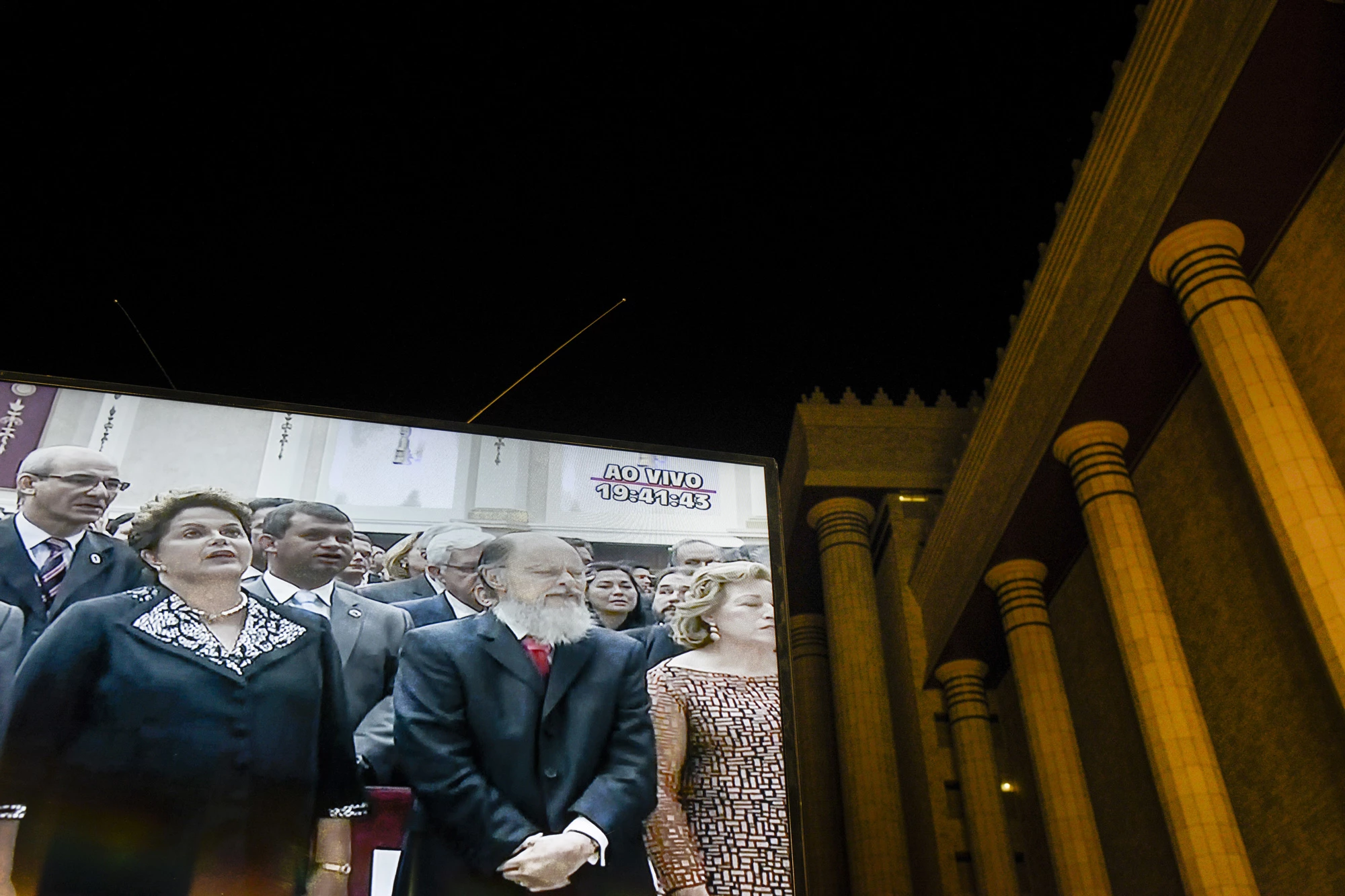 Dilma Rousseff, Brazil's president, front row left, and billionaire Edir Macedo, owner and chairman of Rede Record de Televisao Angola Lda, front row center, are projected on a screen displayed outside a replica of Solomon's Temple during its inauguration ceremony in Sao Paulo, Brazil, on Thursday, July 31, 2014. Billionaire Edir Macedo's temple spans two city blocks and cost 680 million reais ($300 million) to erect. Macedo's net worth has grown to $1.5 billion since he bought the Record TV network in 1989 with a $45 million interest-free loan from the Universal Church of the Kingdom of God, which he founded, according to the Bloomberg Billionaires Index. Photographer: Paulo Fridman/Bloomberg via Getty Images