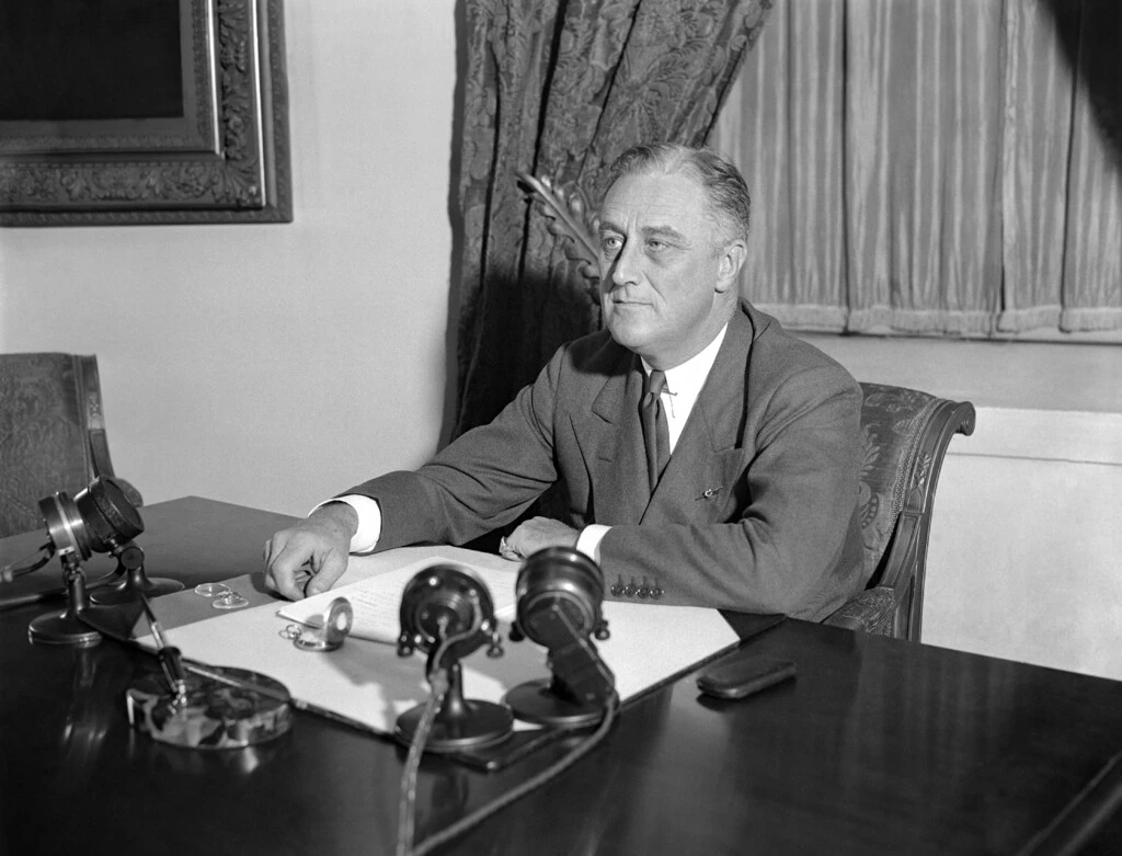 O presidente Franklin D. Roosevelt em sua mesa na Casa Branca, em Washington, quando ele delineou suas ideias para a nação em uma parceria entre o governo e a agricultura, indústria, e transporte, em 7 de maio de 1933.