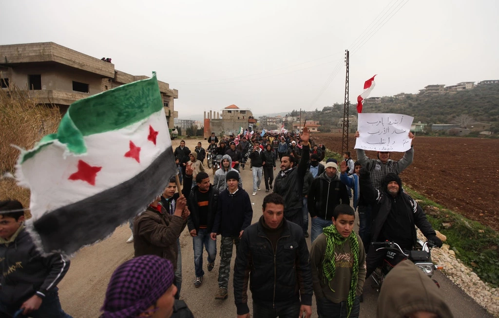 Manifestantes nas ruas de Wadi Khaled, na fronteira entre Líbano e Síria, durante um protesto contra o governo sírio, no dia 30 de dezembro de 2011, agitam uma antiga bandeira da Síria e um cartaz debochando do presidente Bashar al-Assad.