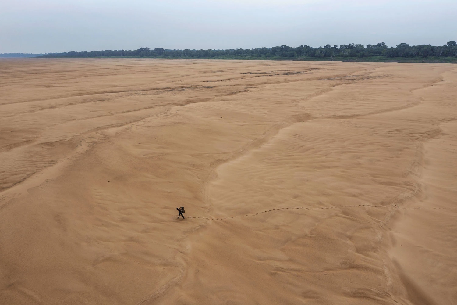 Pescador atravessa caminhando leito seco do rio Solimões, em Tefé (AM); indígenas da região vivem isolamento, com o igarapé fétido, e adoecem por consumirem água barrenta. Foto: Lalo de Almeida/ Folhapress