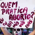 Manifestante com o rosto pintado de Catrina segura cartaz com as palavras "Quem pratica aborto? Eu, tu, ela, nós, vós, elas".