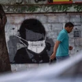 A man walks past a graffiti of Brazilian President Jair Bolsonaro wearing a face mask in downtown Rio de Janeiro, Brazil, on March 24, 2020 during the coronavirus COVID-19 pandemic. - The Rio de Janeiro state government is requesting people not to go to the beach or any other public areas as a measure to contain the coronavirus pandemic. (Photo by Mauro PIMENTEL / AFP) (Photo by MAURO PIMENTEL/AFP via Getty Images)