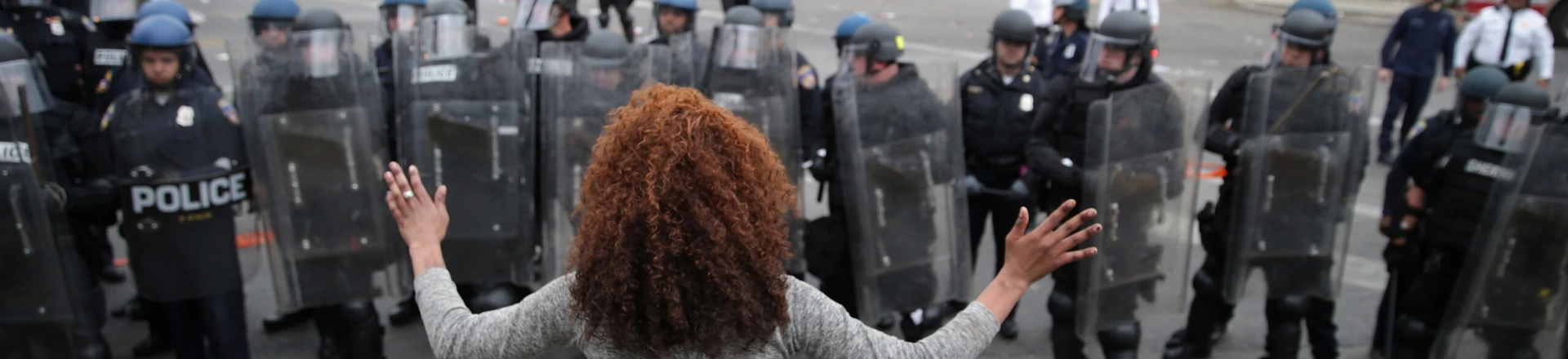 BALTIMORE, MD - APRIL 27:  A woman faces down a line of Baltimore Police officers in riot gear during violent protests following the funeral of Freddie Gray April 27, 2015 in Baltimore, Maryland. Gray, 25, who was arrested for possessing a switch blade knife April 12 outside the Gilmor Homes housing project on Baltimore's west side. According to his attorney, Gray died a week later in the hospital from a severe spinal cord injury he received while in police custody.  (Photo by Chip Somodevilla/Getty Images)