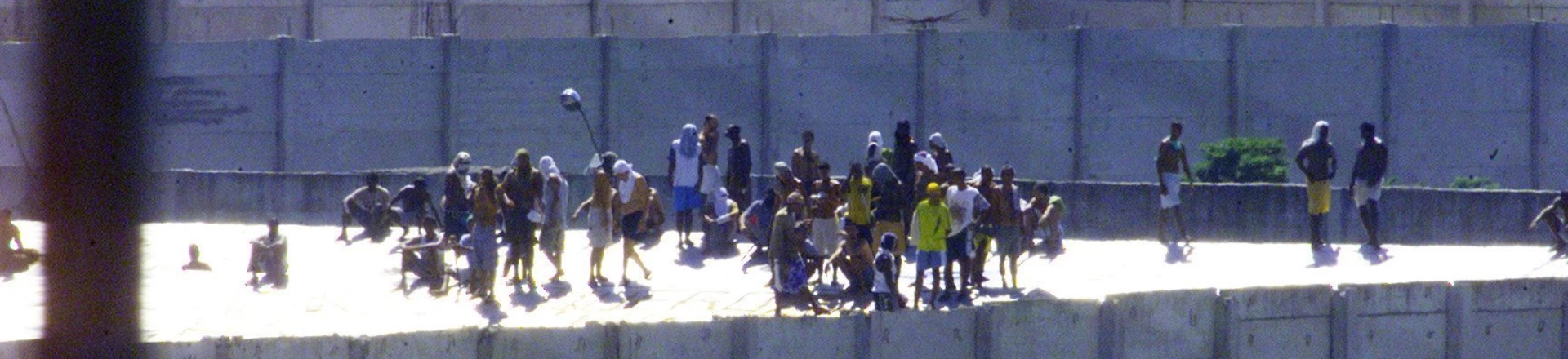 Presos rebelados no telhado da Casa de Custódia Pedro Mello da Silva, no Complexo Penitenciário de Bangu. O presídio tem capacidade para 500 presos à espera de julgamento, mas abrigava 375. Os detentos renderam sete policiais e os amarraram a botijões de gás. O objetivo dos presos era uma fuga em massa; cerca de 30 conseguiram fugir. (Rio de Janeiro, RJ, 20.01.2003. Foto: Alexandre Campbell/Folhapress) Presos rebelados no telhado da Casa de Custódia Pedro Mello da Silva, no Complexo Penitenciário de Bangu. O presídio tem capacidade para 500 presos à espera de julgamento, mas abrigava 375. Os detentos renderam sete policiais e os amarraram a botijões de gás. O objetivo dos presos era uma fuga em massa; cerca de 30 conseguiram fugir. (Rio de Janeiro, RJ, 20.01.2003. Foto: Alexandre Campbell/Folhapress)