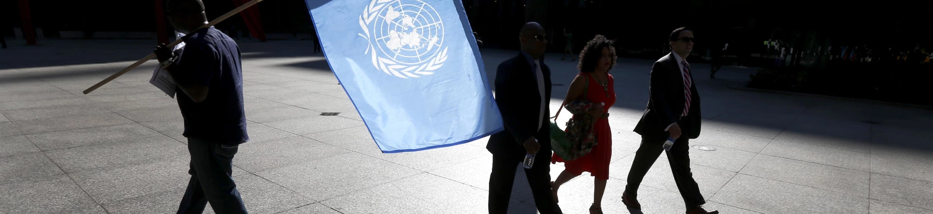 A protester is silhouetted as he carries the United Nations flag during a rally against Nigerian President Buhari as pedestrians walk through federal plaza Wednesday, Sept. 20, 2017, in Chicago. (AP Photo/Charles Rex Arbogast)