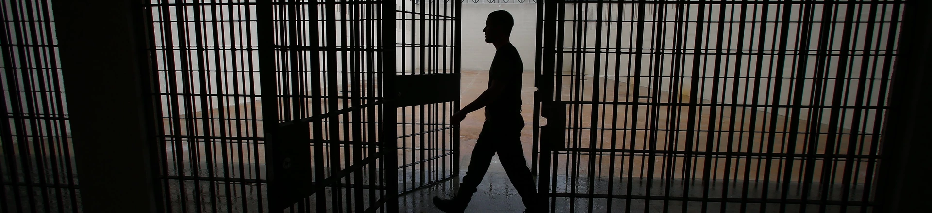 Homem atravessa área de presídio com imagem em penumbra. Homem atravessa área de presídio com imagem em penumbra.