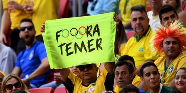A man holds a sign against Brazil's acting President Michel Temer during the Rio 2016 Olympic Games First Round Group A men's football match Brazil vs South Africa, at the Mane Garrincha Stadium in Brasilia on August 4, 2016. / AFP / EVARISTO SA        (Photo credit should read EVARISTO SA/AFP/Getty Images)