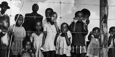 A group of children (and a few men) gaze from behind a barbed-wire fence that marks the boundary of the Moroka township in Soweta, Johannesburg, South Africa, April 21, 1950. (Photo by Margaret Bourke-White/The LIFE Picture Collection via Getty Images)