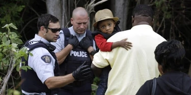 A Haitian boy holds onto his father as they approach an illegally crossing point, staffed by Royal Canadian Mounted Police officers, from Champlain, N.Y., to Saint-Bernard-de-Lacolle, Quebec, Monday, Aug. 7, 2017. Seven days a week, 24-hours a day people from across the globe are arriving at the end of a New York backroad so they can walk across a ditch into Canada knowing they will be instantly arrested, but with the hope the Canadian government will be kinder to them than the United States. (AP Photo/Charles Krupa)