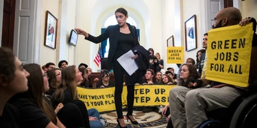 Alexandria Ocasio-Cortez fala com ativistas do movimento Sunrise Movement que protestam nos escritórios da líder da minoria da Câmara, Nancy Pelosi, em Washington D.C., em 13 de novembro. Alexandria Ocasio-Cortez fala com ativistas do movimento Sunrise Movement que protestam nos escritórios da líder da minoria da Câmara, Nancy Pelosi, em Washington D.C., em 13 de novembro.
