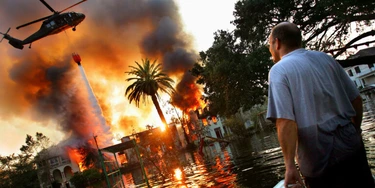 UNITED STATES - SEPTEMBER 04:  A man watches a house burn on Napolean St. as helicopters try to extinguish the fire by dropping water from above in Hurricane Katrina ravaged New Orleans. Because of the extensive flooding caused by the breaking of the city's levies, fire trucks were unable to reach burning homes and in some cases whole blocks burned to the ground.  (Photo by Craig Warga/NY Daily News Archive via Getty Images)