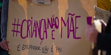 Foto de banner em protesto sobre aborto com as palavras "criança não é mãe e estuprador não é pai" pintadas.