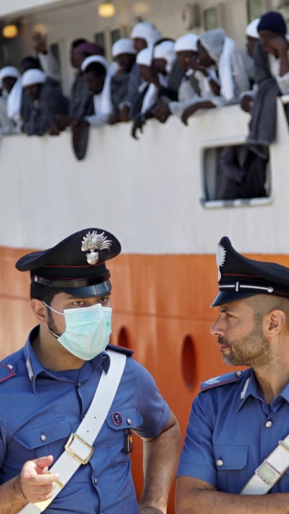 Two port security officers stand in front of the 'Aquarius' vessel as migrants wait for disembarking after arriving to Messina, Sicily island, Italy, Sunday. June 26, 2016. A group of more than 650 migrants arrived in Messina after being rescued on the Mediterranean Sea earlier this week. (AP Photo/Bram Janssen)
