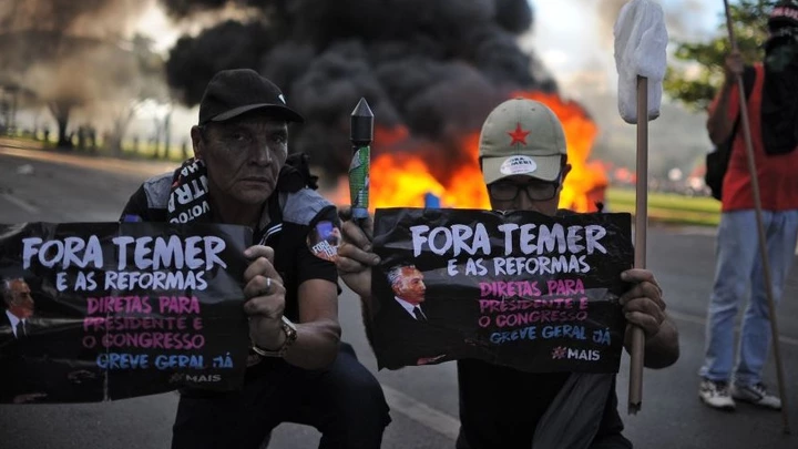 Demonstrators hold banners against Brazilian President Michel temer during clashes in the protest "Occupy Brasilia" against the labor and social security reforms of his government in Brasilia, on May 24, 2017. / AFP PHOTO / Andressa Anholete        (Photo credit should read ANDRESSA ANHOLETE/AFP/Getty Images) Demonstrators hold banners against Brazilian President Michel temer during clashes in the protest "Occupy Brasilia" against the labor and social security reforms of his government in Brasilia, on May 24, 2017. / AFP PHOTO / Andressa Anholete        (Photo credit should read ANDRESSA ANHOLETE/AFP/Getty Images)
