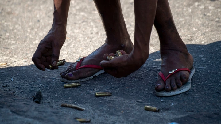 A resident of the Complex do Alemao favela collects cases on Itaoca Avenue as Rio de Janeiro's Military Police Special Unit (Choque) carries out an operation at the slum, in Rio, Brazil, on July 16, 2018. (Photo by Mauro PIMENTEL / AFP)        (Photo credit should read MAURO PIMENTEL/AFP via Getty Images)