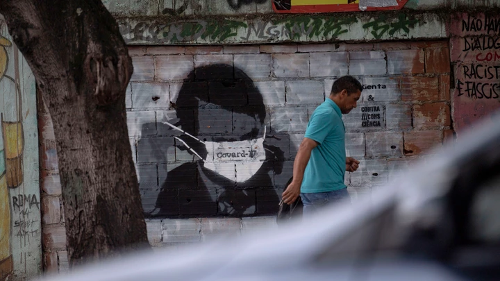 A man walks past a graffiti of Brazilian President Jair Bolsonaro wearing a face mask in downtown Rio de Janeiro, Brazil, on March 24, 2020 during the coronavirus COVID-19 pandemic. - The Rio de Janeiro state government is requesting people not to go to the beach or any other public areas as a measure to contain the coronavirus pandemic. (Photo by Mauro PIMENTEL / AFP) (Photo by MAURO PIMENTEL/AFP via Getty Images)