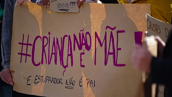 Foto de banner em protesto sobre aborto com as palavras "criança não é mãe e estuprador não é pai" pintadas.